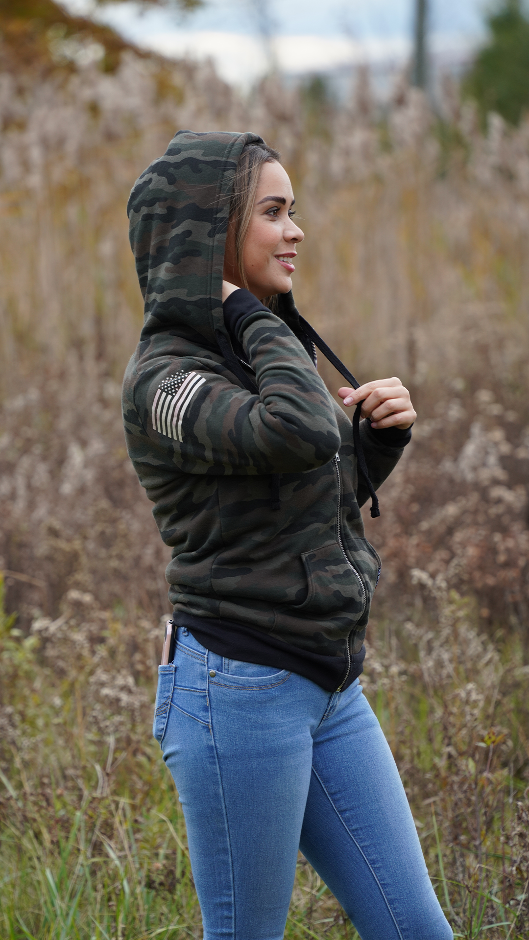 FEMALE WEARING MILITARY HOODIE IN THE FIELD AMERICAN FLAG ON THE RIGHT SHOULDER